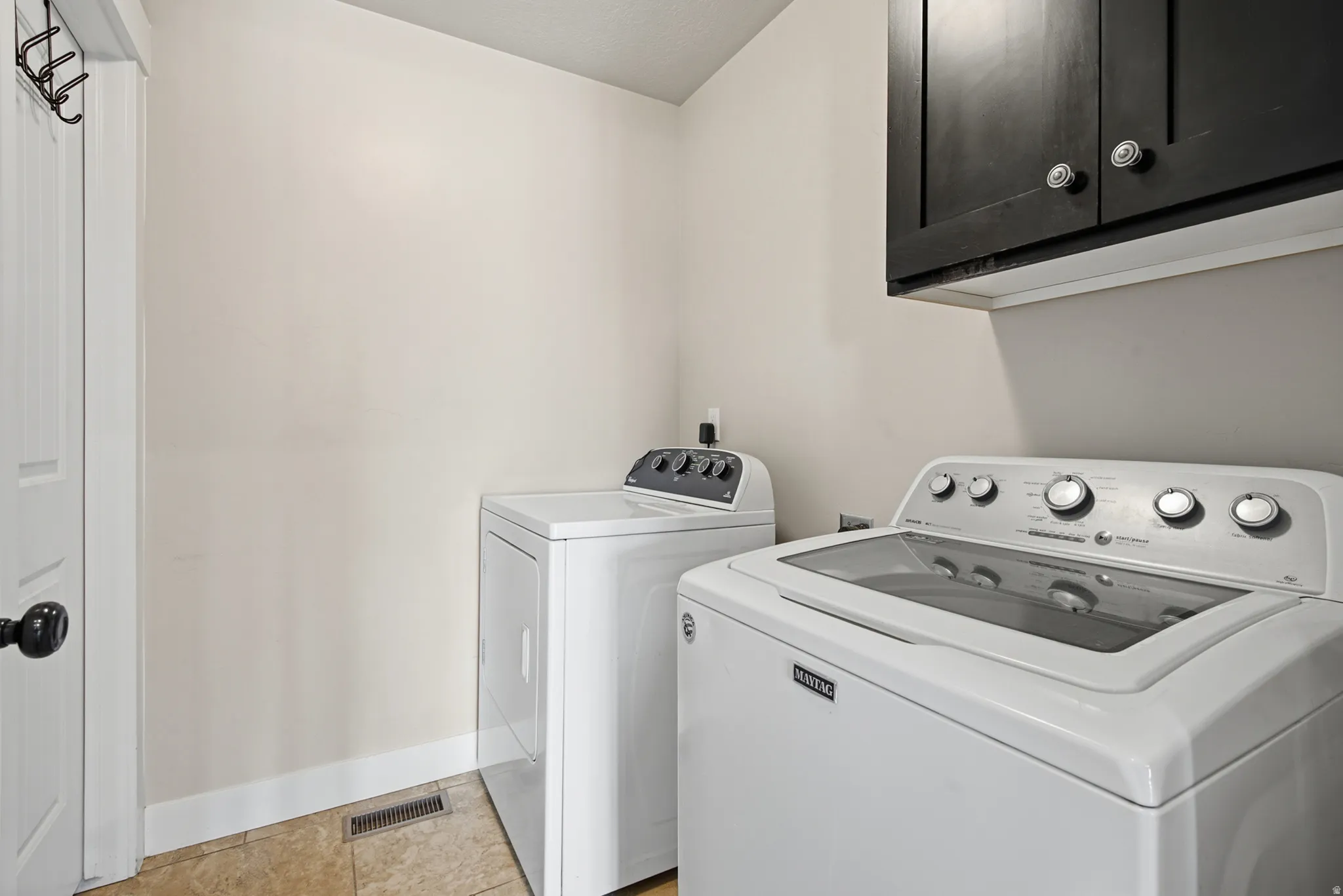 Laundry area featuring tile flooring, white walls, and a dark overhead cabinet with circular hardware