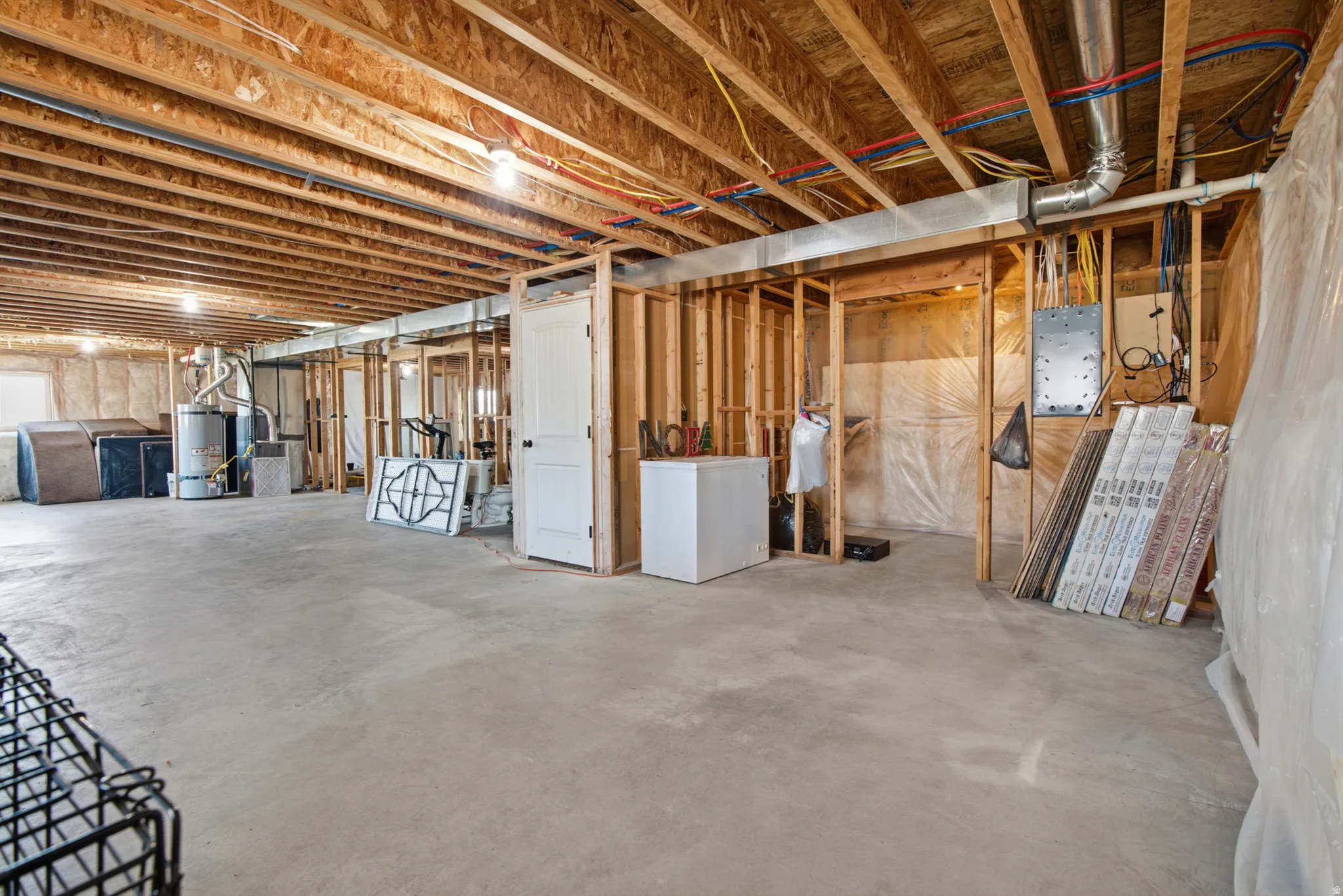 Unfinished basement with exposed wood joists and framing, concrete flooring, and visible plumbing and electrical infrastructure
