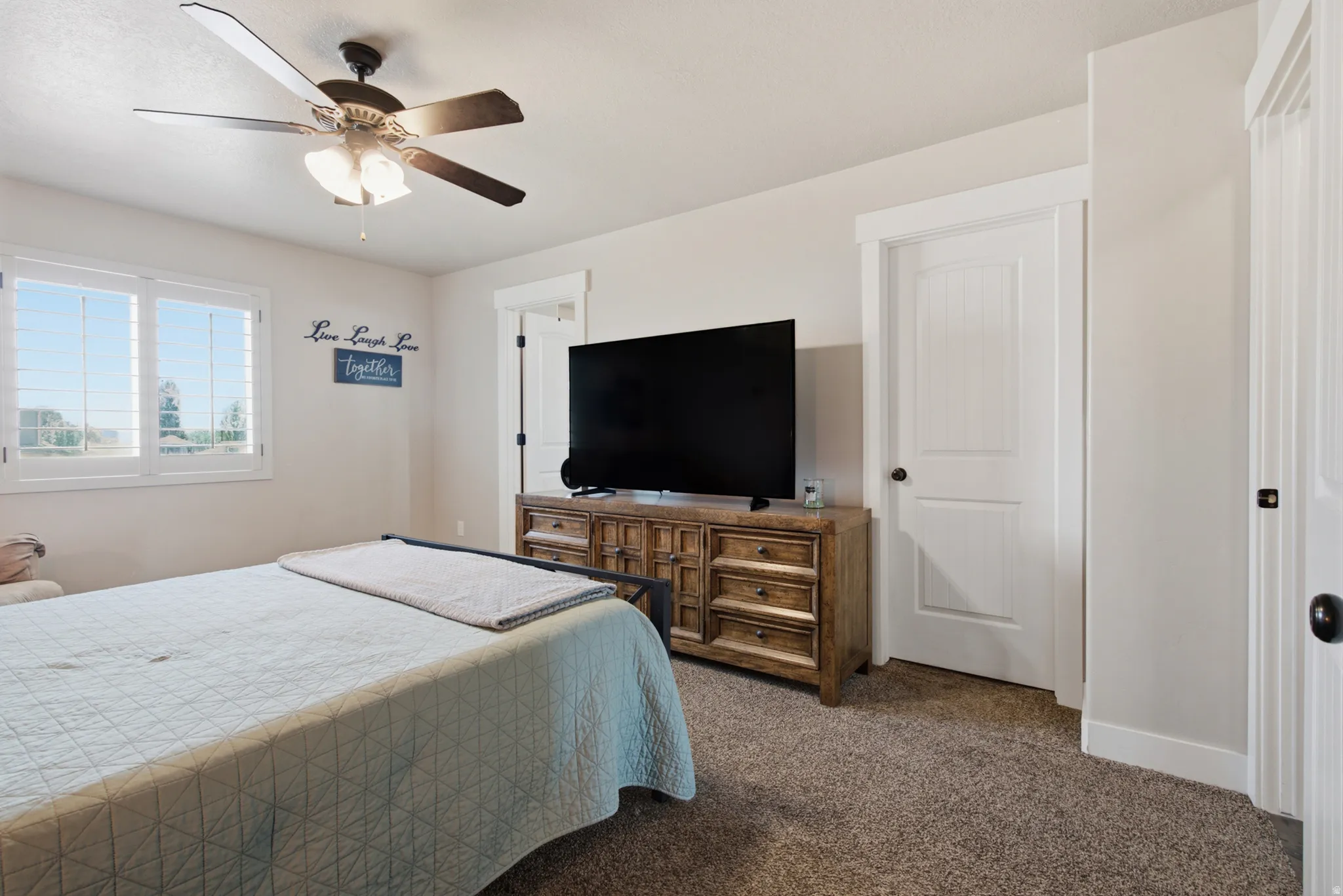Carpeted room featuring a ceiling fan, window with white plantation shutters, and a white paneled door