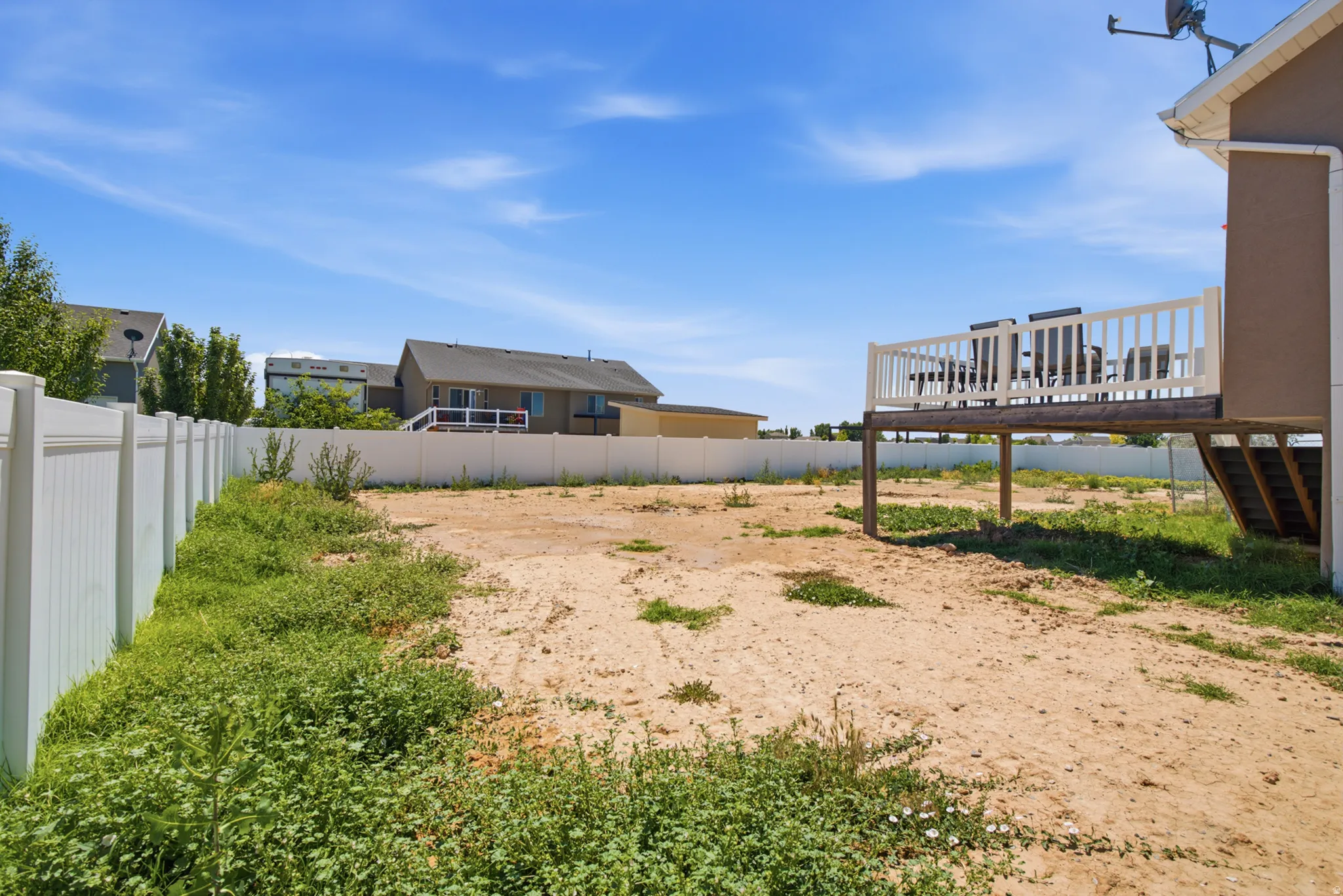 Spacious backyard featuring a raised deck with white railing, vinyl perimeter fencing, and ample open ground