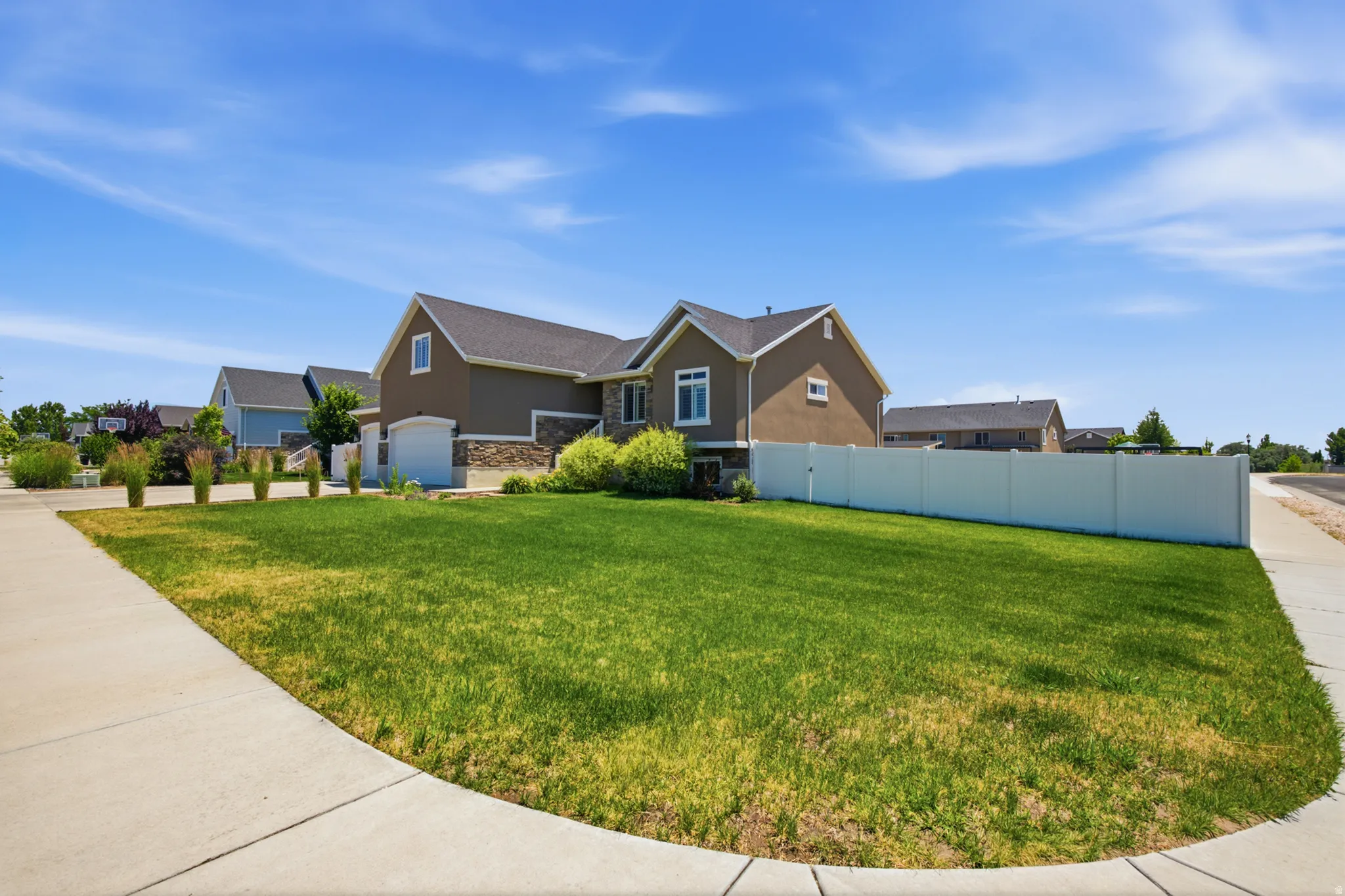 Exterior facade featuring light brown stucco and stone accents, a dark shingle roof, a two-car garage, and a white privacy fence