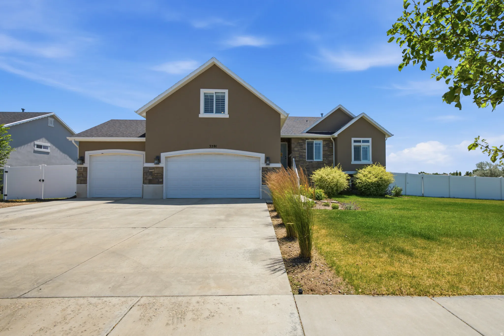Front exterior featuring stucco siding, stone accents, two attached garages with arched entryways, and a concrete driveway