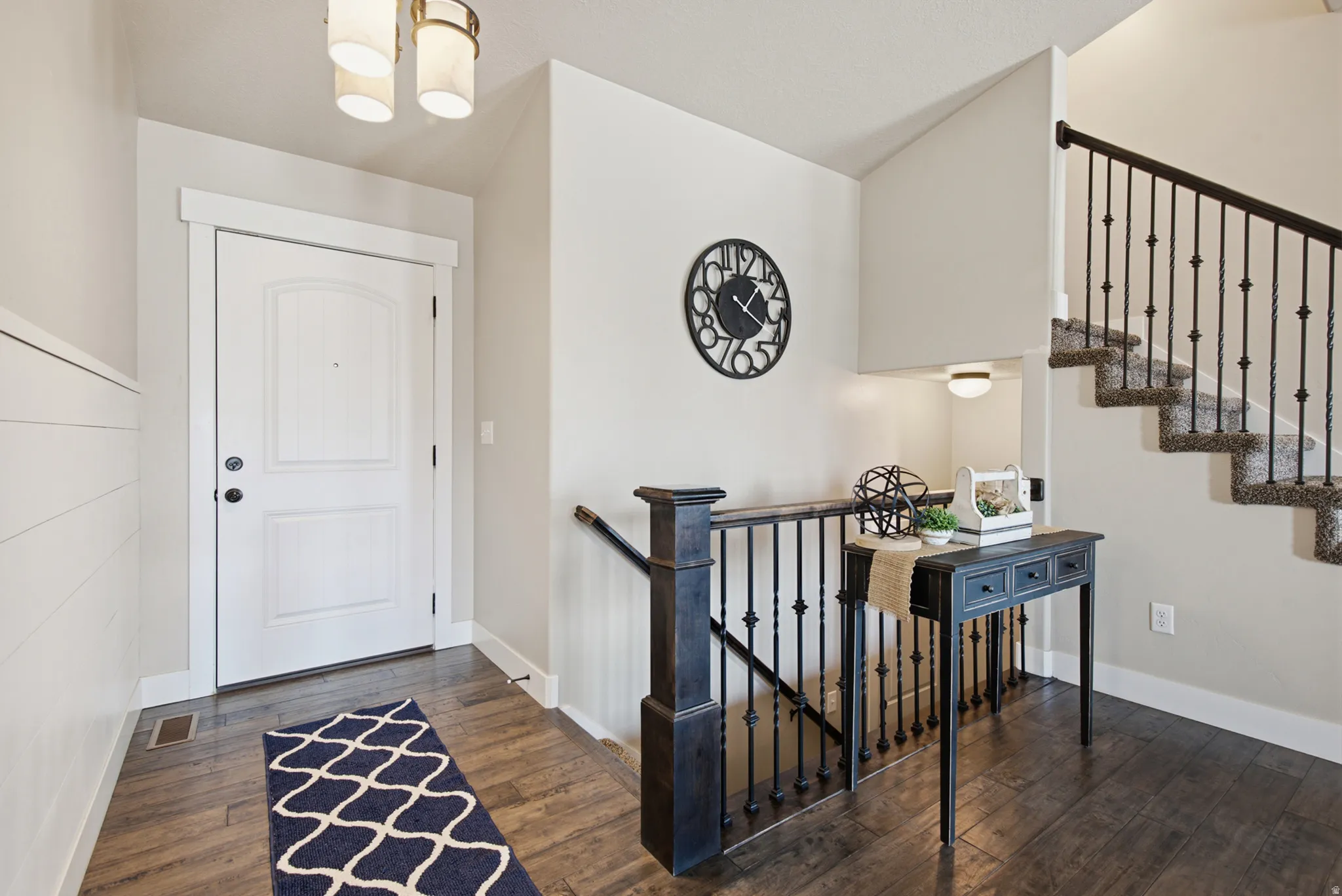 Entryway featuring wood-finish flooring, white shiplap wall paneling, a paneled entry door, and a staircase with black wrought iron balusters and carpeted treads