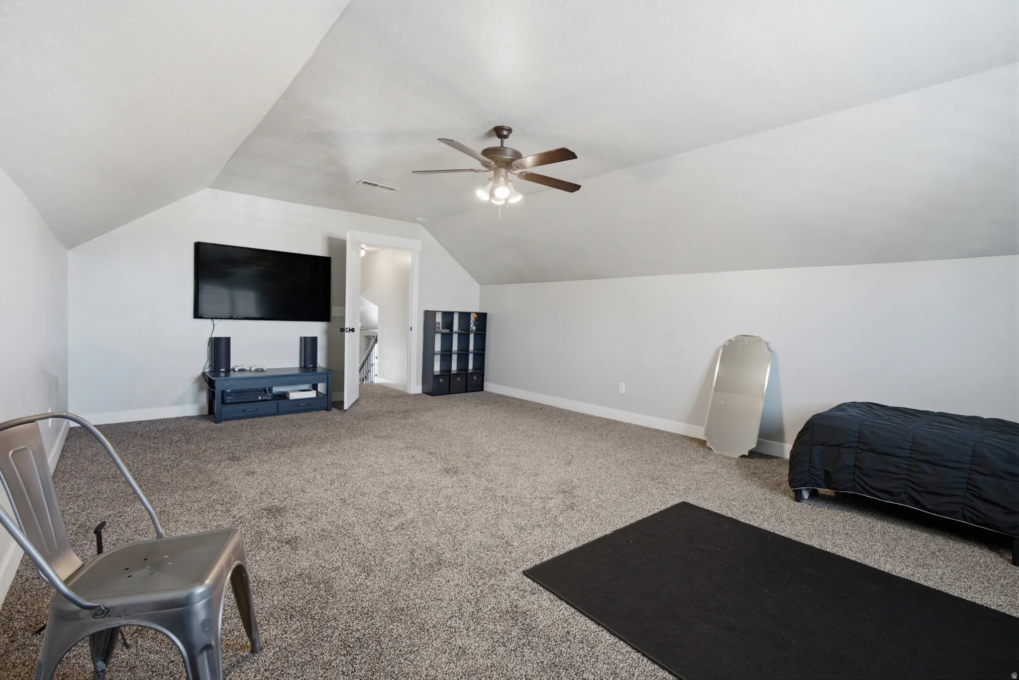 Spacious room featuring vaulted ceilings, neutral-toned carpeting, a ceiling fan with integrated lighting, and white trim