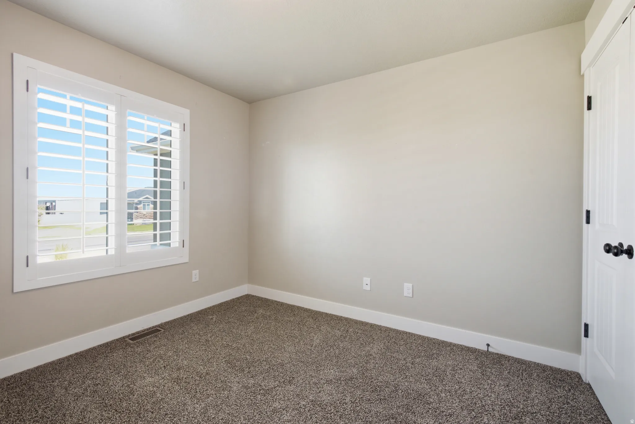 Neutral tone wall color with white plantation shutters, white baseboards, and textured carpet