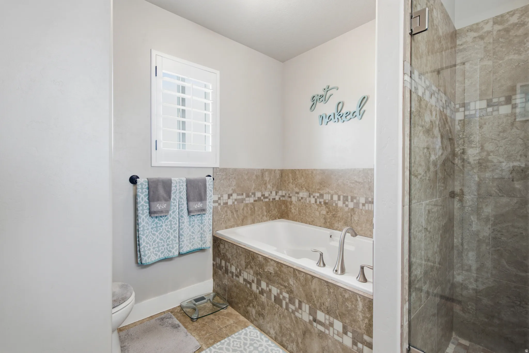 Bathroom featuring a built-in soaking tub with brushed nickel fixtures, a walk-in shower with glass enclosure, white plantation shutters, and extensive tile work on the floor and tub surround