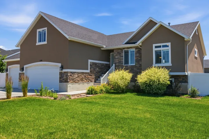 Stucco and stone exterior featuring a two-car garage, white window shutters, and a well-maintained lawn