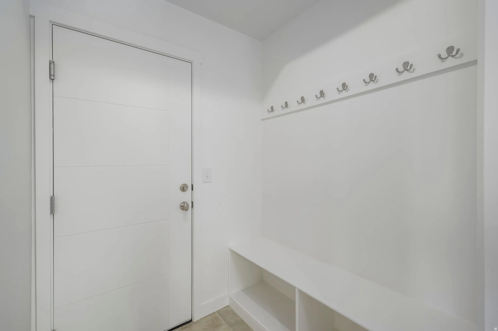 Entryway featuring a modern panel door with horizontal grooves, brushed nickel hardware, and a built-in white bench with open shelving
