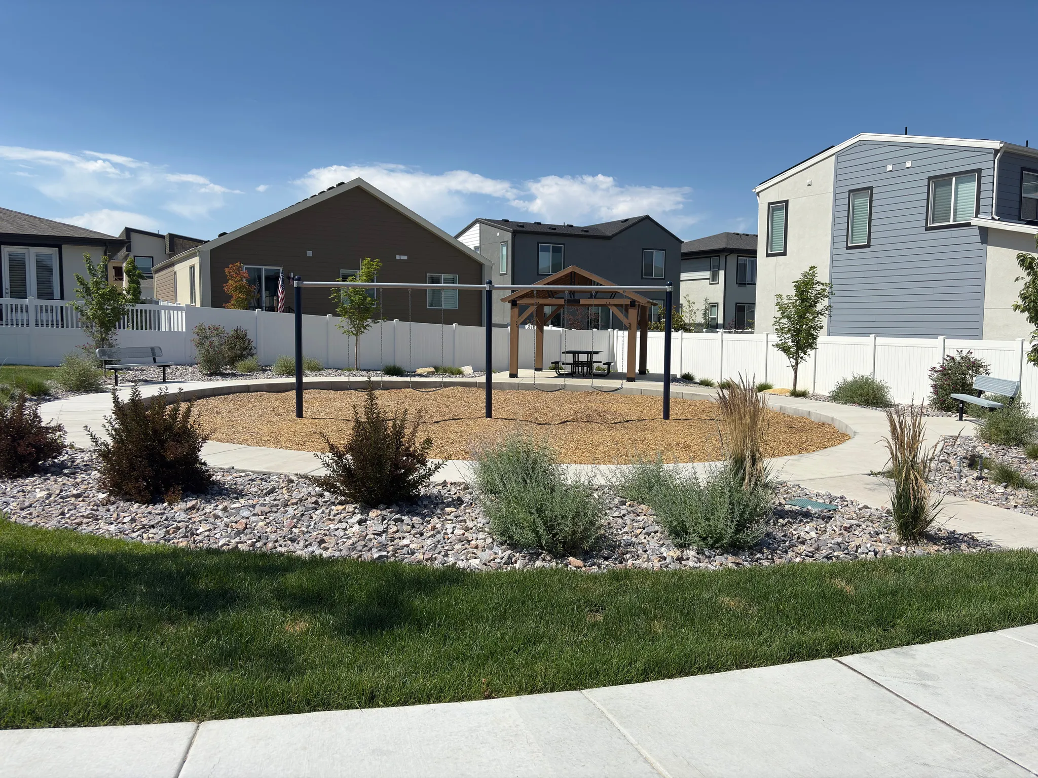 Community park area featuring a central wood chip play surface, a wooden gazebo with a picnic table, and a horizontal bar play structure