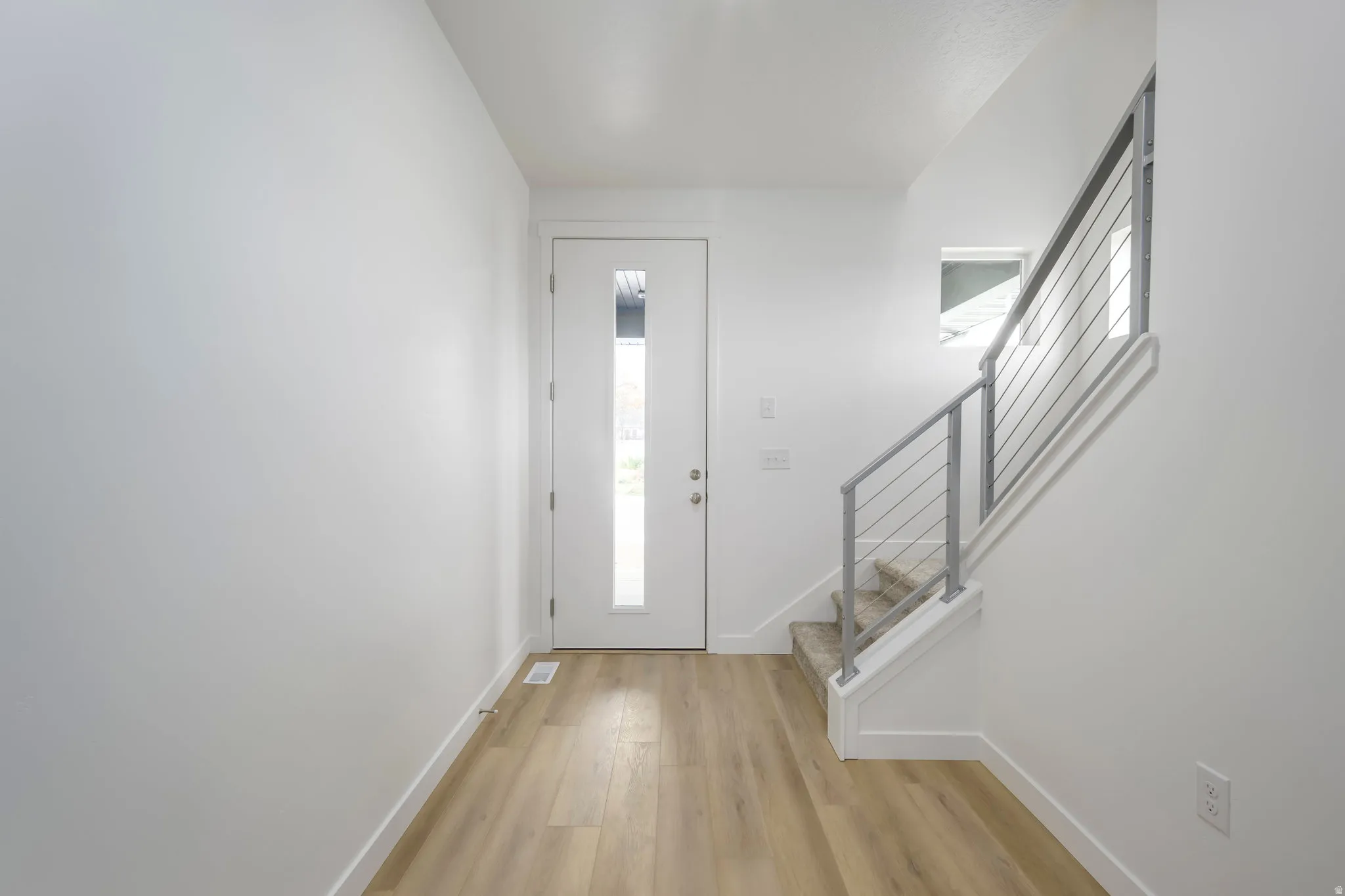 Entryway featuring wood-finish flooring, a white modern door with vertical frosted glass, and a staircase with contemporary metal railing and carpeted treads