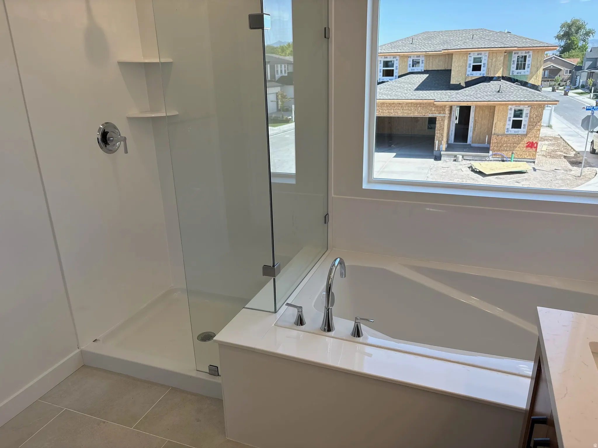 Integrated soaking tub with chrome fixtures, glass-enclosed shower, shower niche shelving, and large window