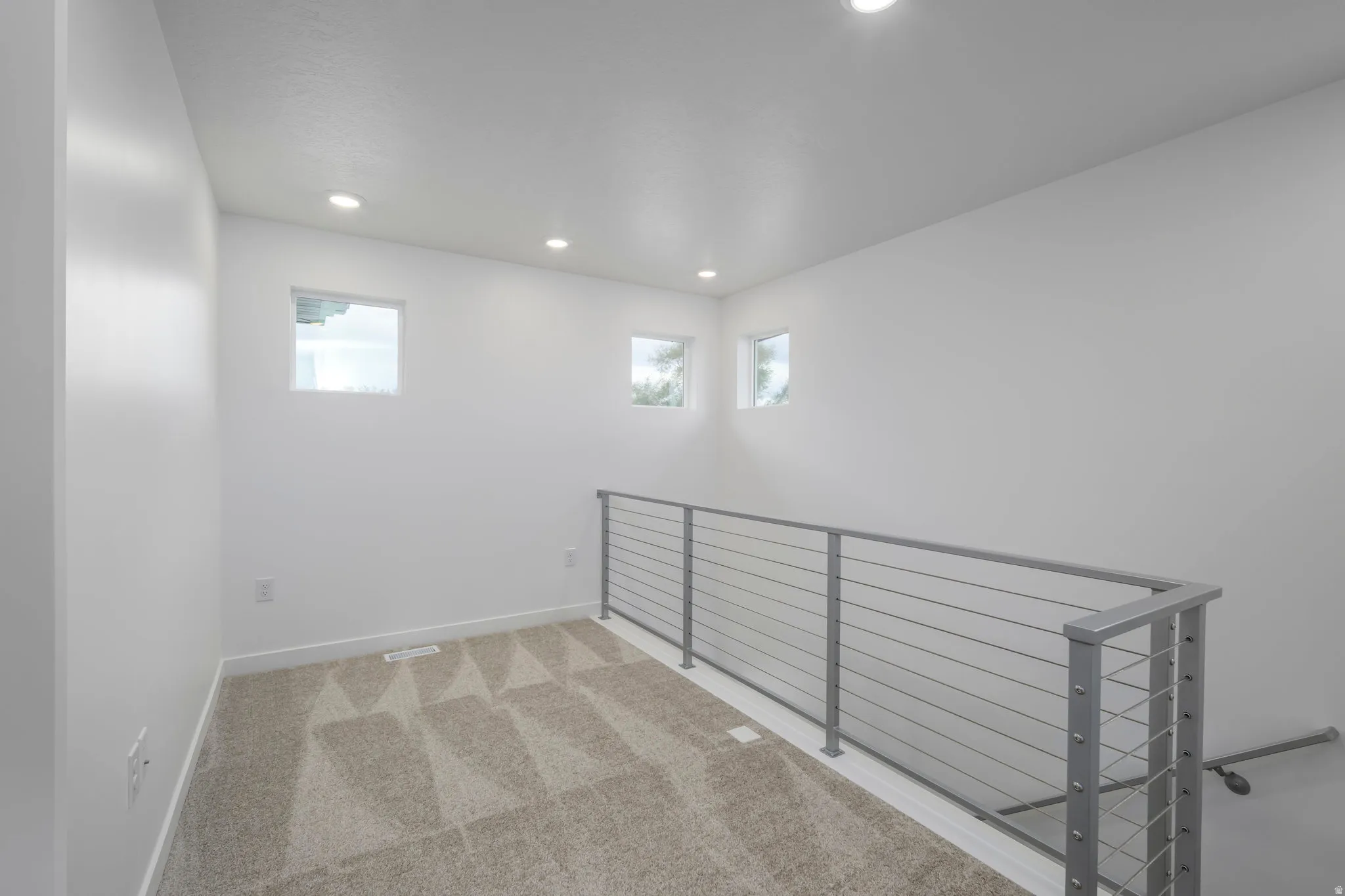 Upper-level landing featuring a modern cable railing system, recessed ceiling lighting, and multiple windows for natural illumination