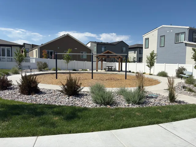 Community park area featuring a central wood chip play surface, a wooden gazebo with a picnic table, and a horizontal bar play structure