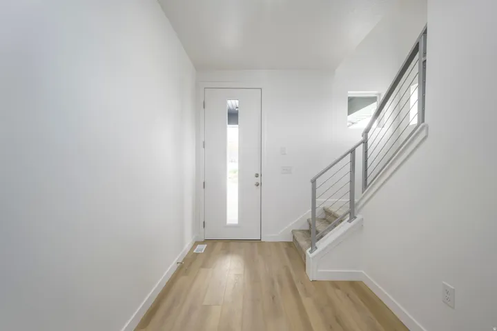 Entryway featuring wood-finish flooring, a white modern door with vertical frosted glass, and a staircase with contemporary metal railing and carpeted treads
