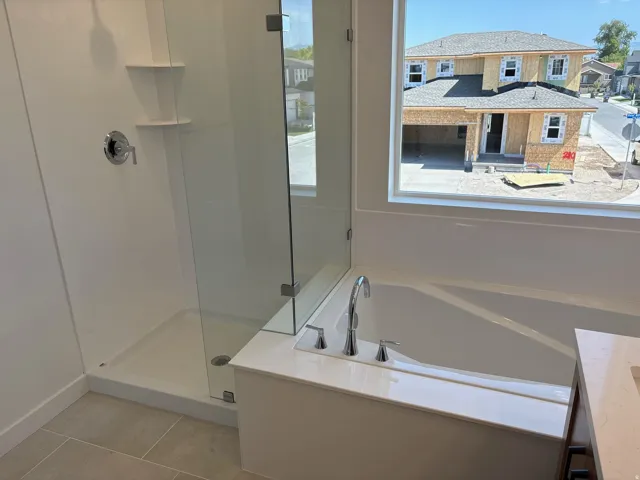 Integrated soaking tub with chrome fixtures, glass-enclosed shower, shower niche shelving, and large window