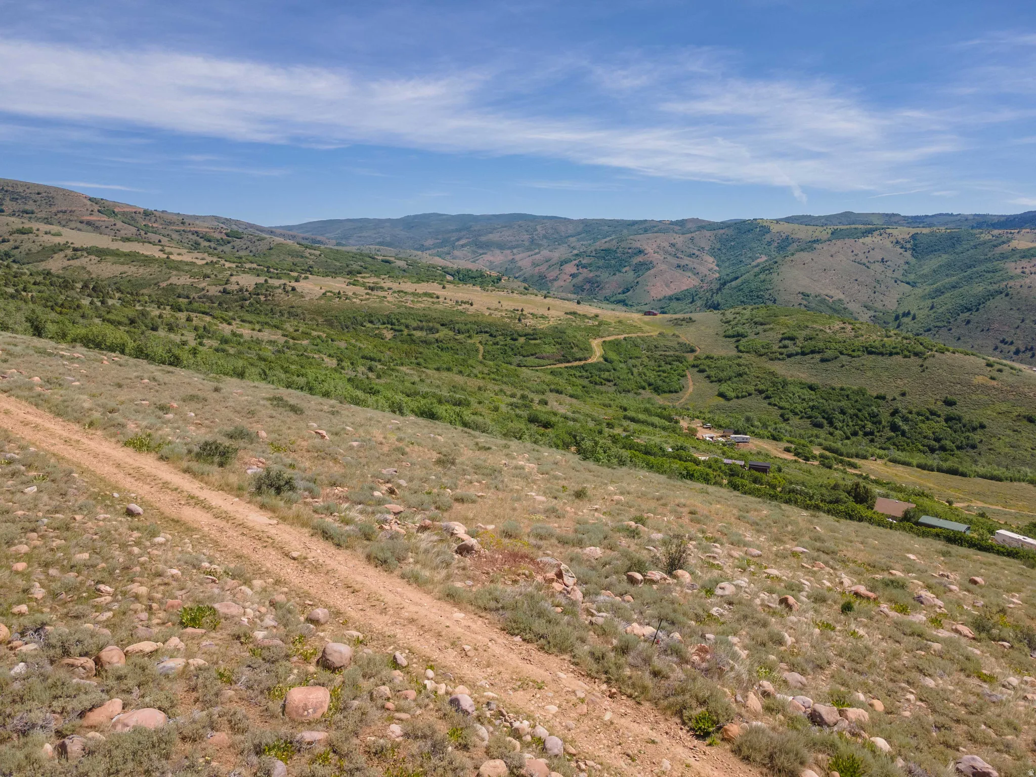 Expansive sloped terrain with a prominent dirt road, scattered boulders, and low-lying vegetation