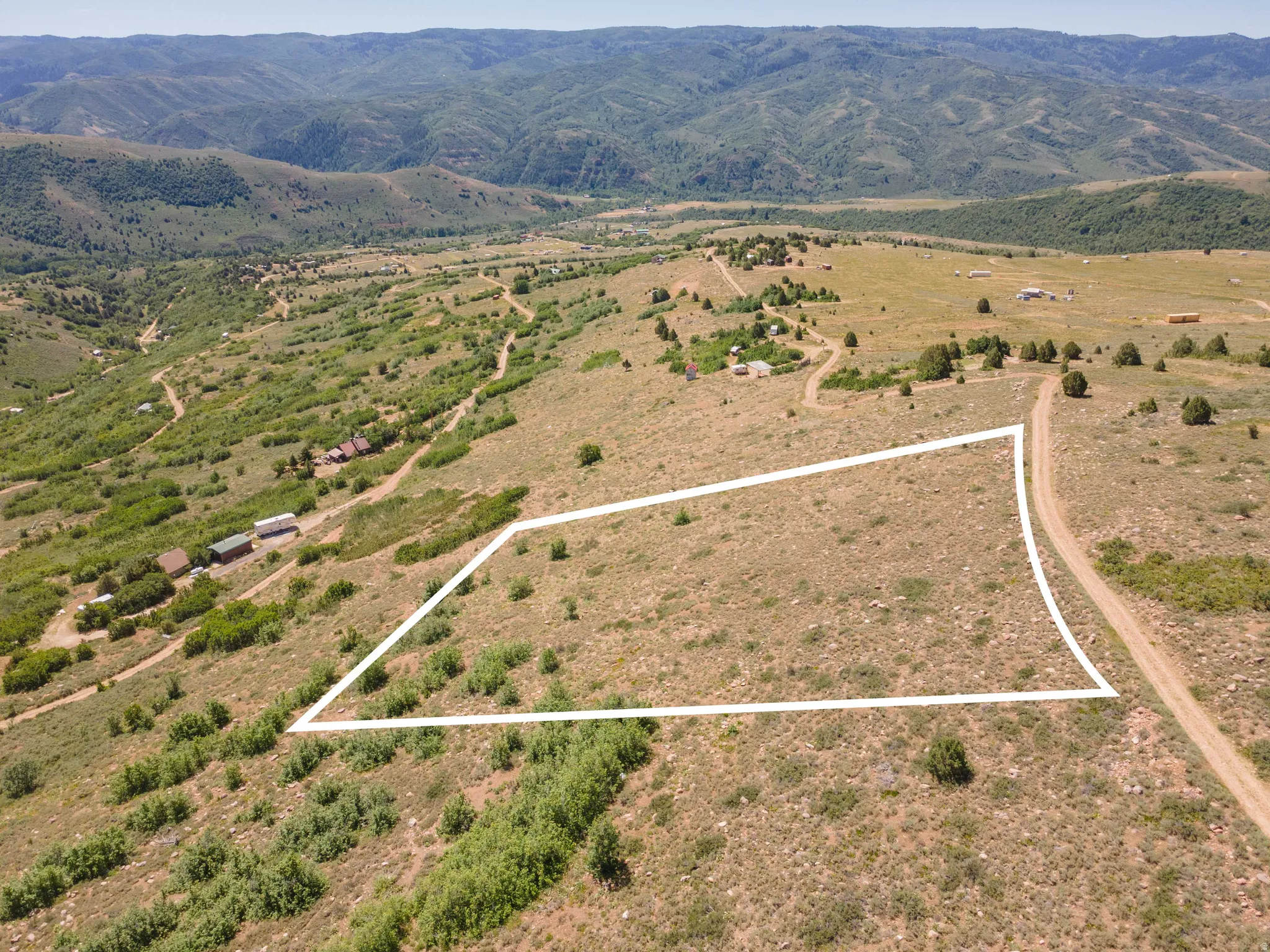 Expansive land parcel featuring a gentle slope, surrounded by undeveloped natural terrain and distant mountains