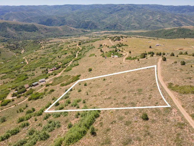 Expansive land parcel featuring a gentle slope, surrounded by undeveloped natural terrain and distant mountains