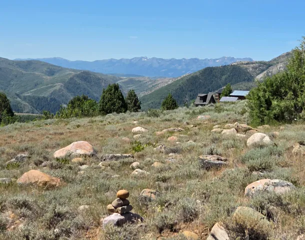 Expansive mountain landscape featuring distant peaks and a partial property structure with a dark-toned roof