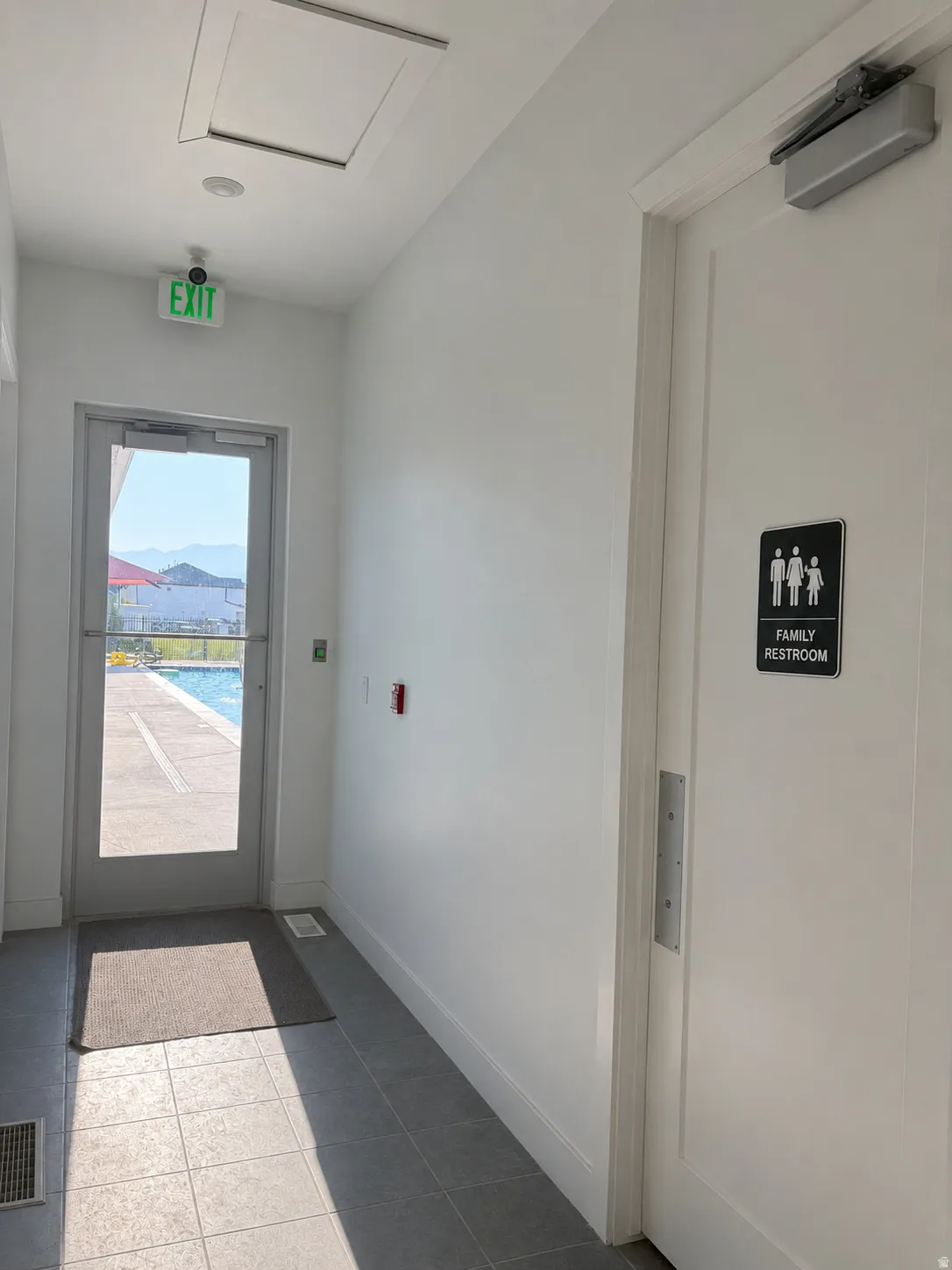 Tiled flooring in a hallway with a glass-paneled exit door and a recessed ceiling light