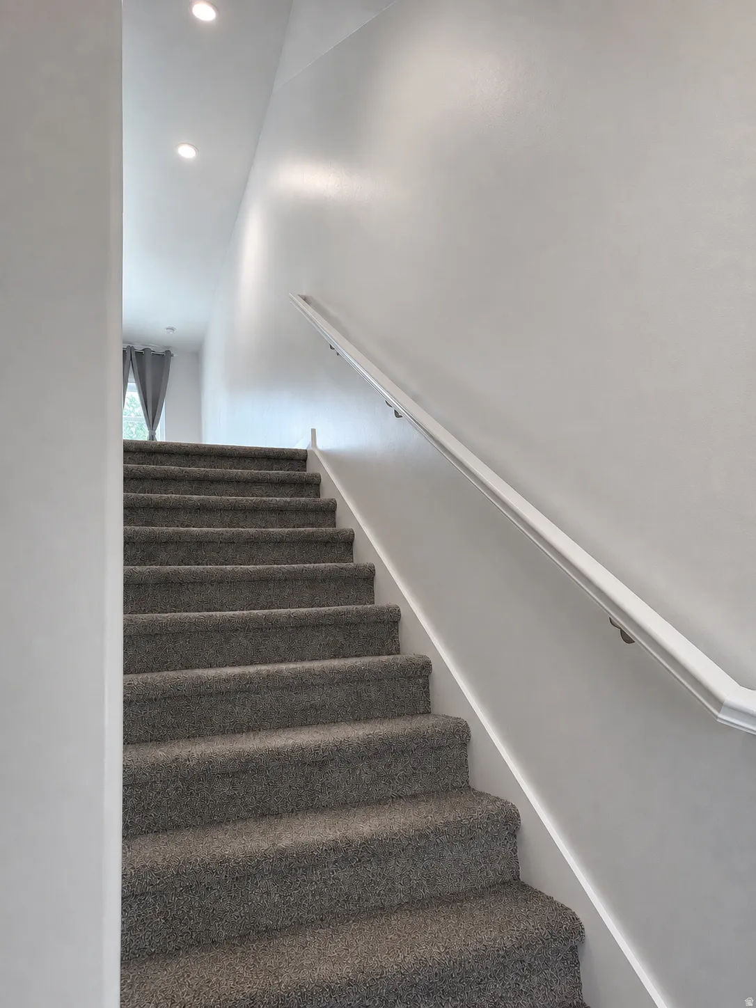 Staircase with gray carpeted steps and a white handrail