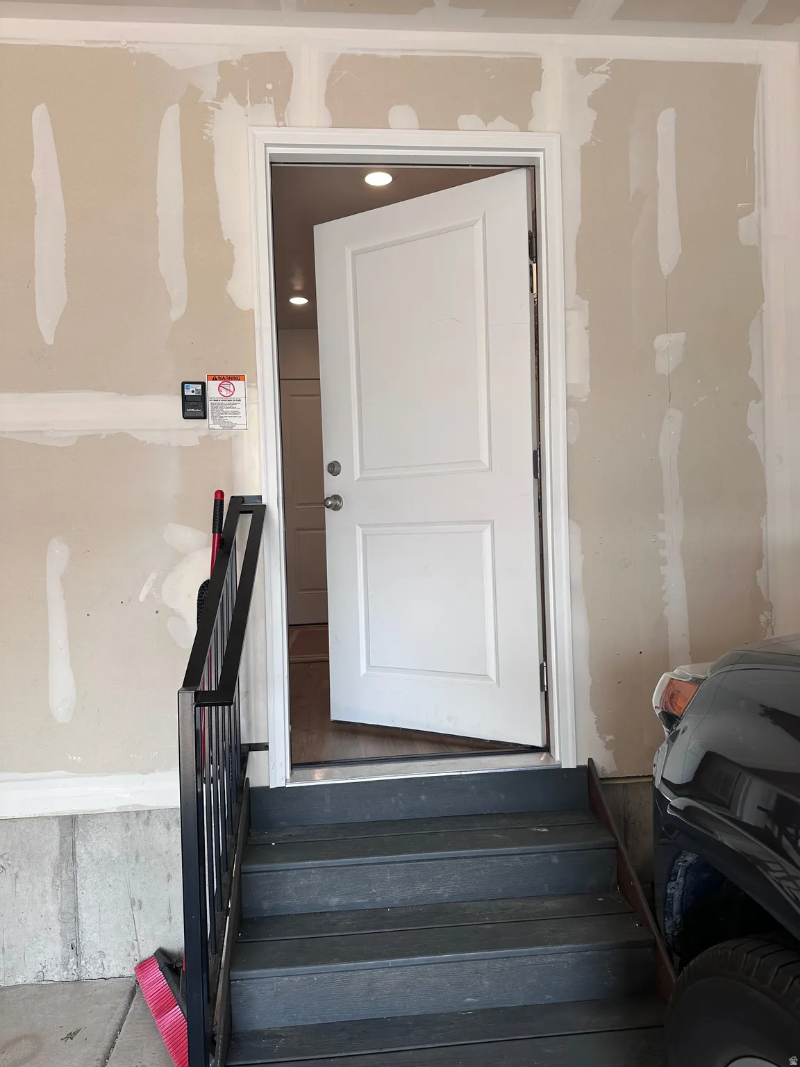 Interior access door with panel detailing, leading to a finished space with recessed lighting and wood-finish flooring