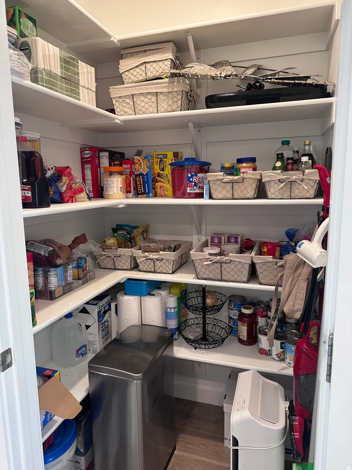 Walk-in pantry featuring white shelving, wood-finish flooring, and ample storage space