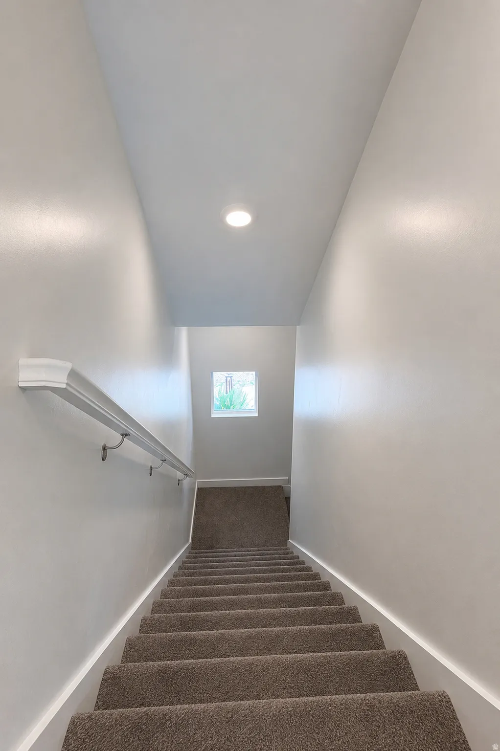 Carpeted staircase with recessed lighting and a window at the landing