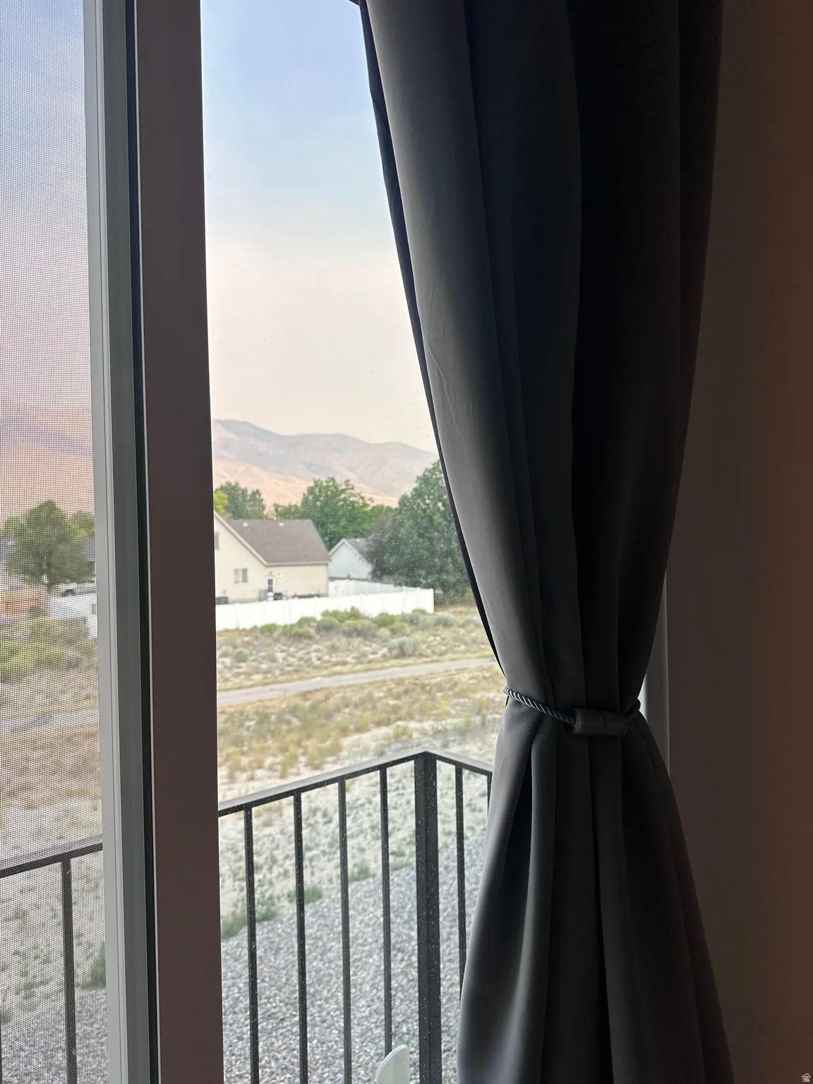 Sliding glass door with an integrated screen and a black metal balcony railing, offering a distant mountain backdrop