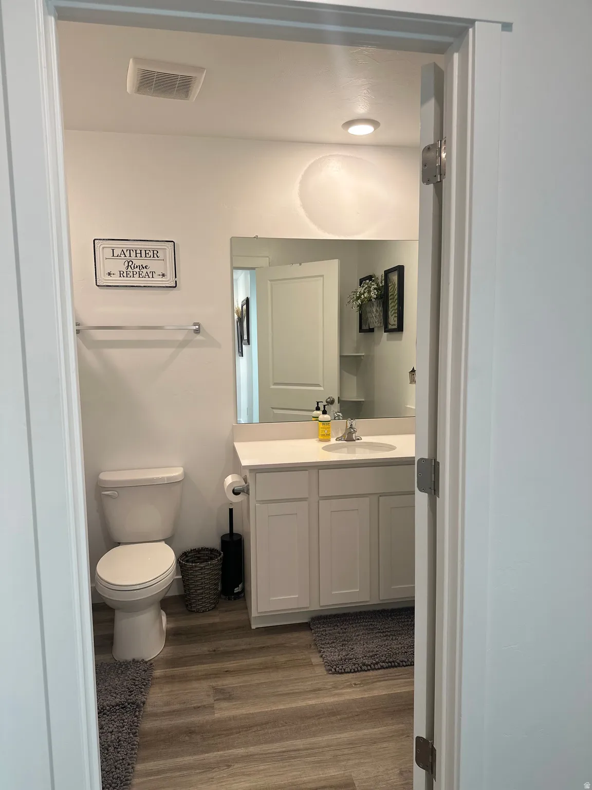 Bathroom featuring wood-finish flooring, a white vanity with paneled doors, a white countertop, and a single basin sink