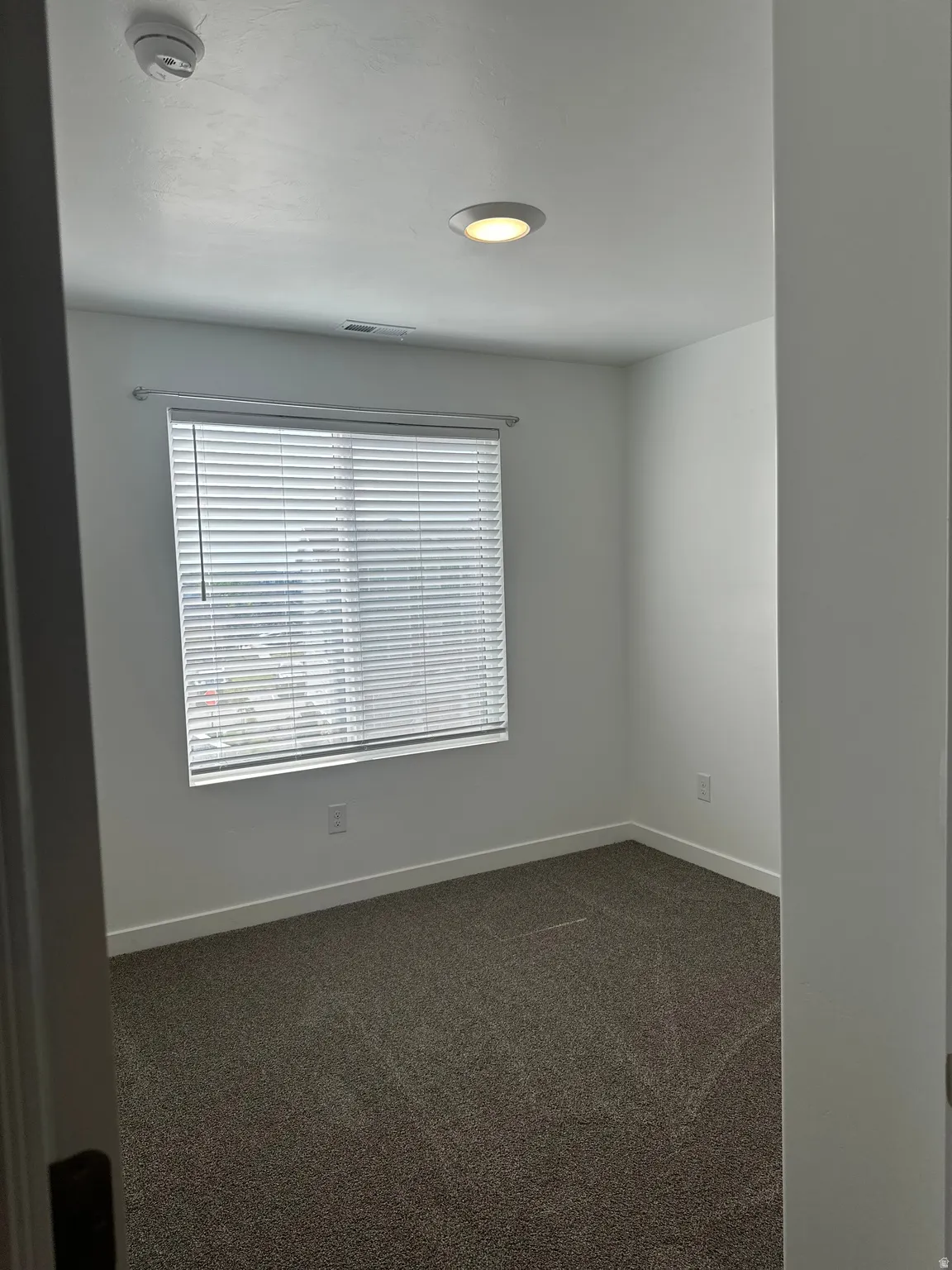 Room featuring neutral wall paint, recessed lighting, a window with horizontal blinds, textured carpet flooring, and white baseboards