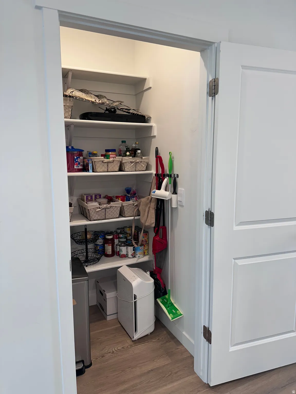 Spacious pantry with multiple built-in shelves, wood-finish flooring, and bright interior lighting