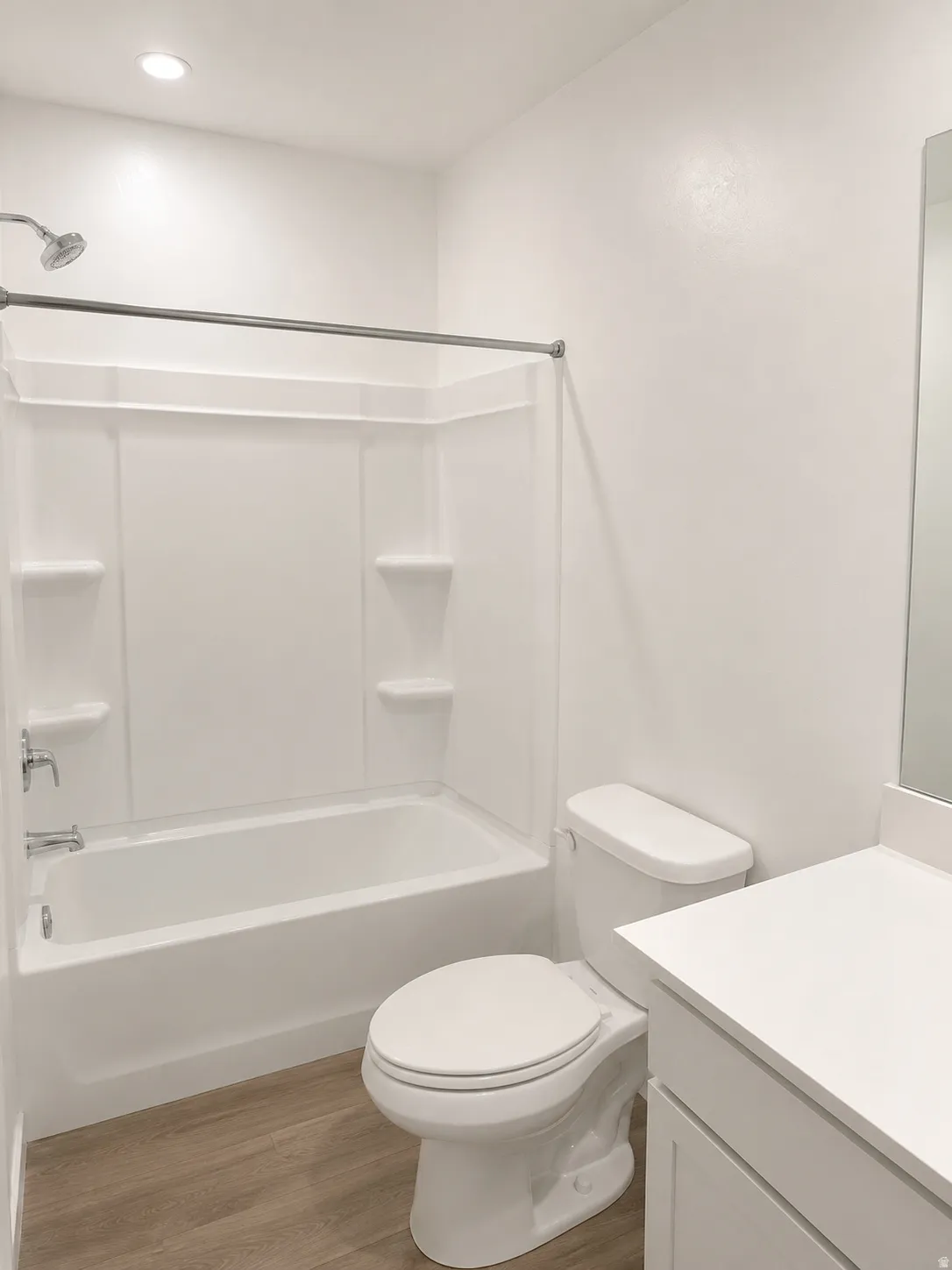 Contemporary bathroom featuring a white tub/shower combination with integrated shelving, a white toilet, and a vanity with a white countertop and cabinet