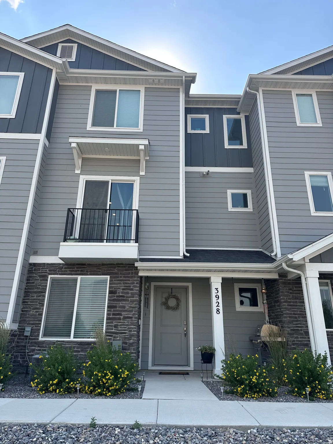 Contemporary townhome facade featuring gray siding, dark stone veneer accents, and a black wrought iron balcony