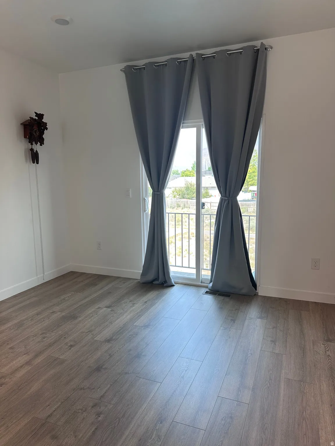 Spacious room featuring wood-finish flooring, recessed ceiling lighting, and a sliding glass door leading to an outdoor area with a black metal railing