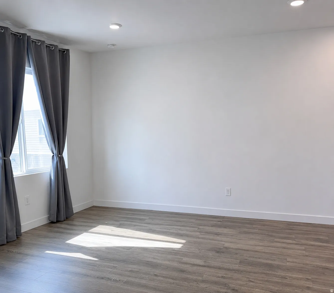 Spacious room featuring wood-finish flooring, recessed lighting, white walls, and bright windows