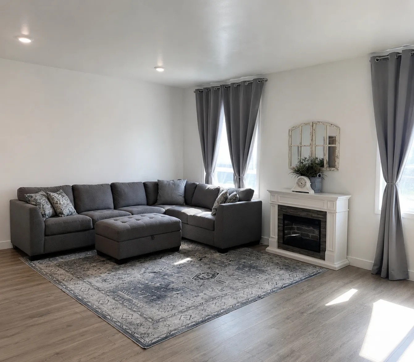 Spacious living area featuring light wood-finish flooring, recessed lighting, and a white decorative fireplace with a dark-tiled firebox