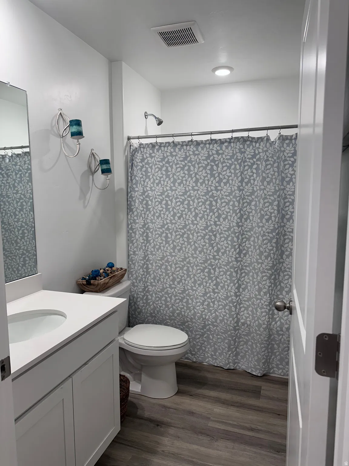 Well-lit bathroom featuring a white vanity with an integrated sink, a commode, and a shower with a showerhead
