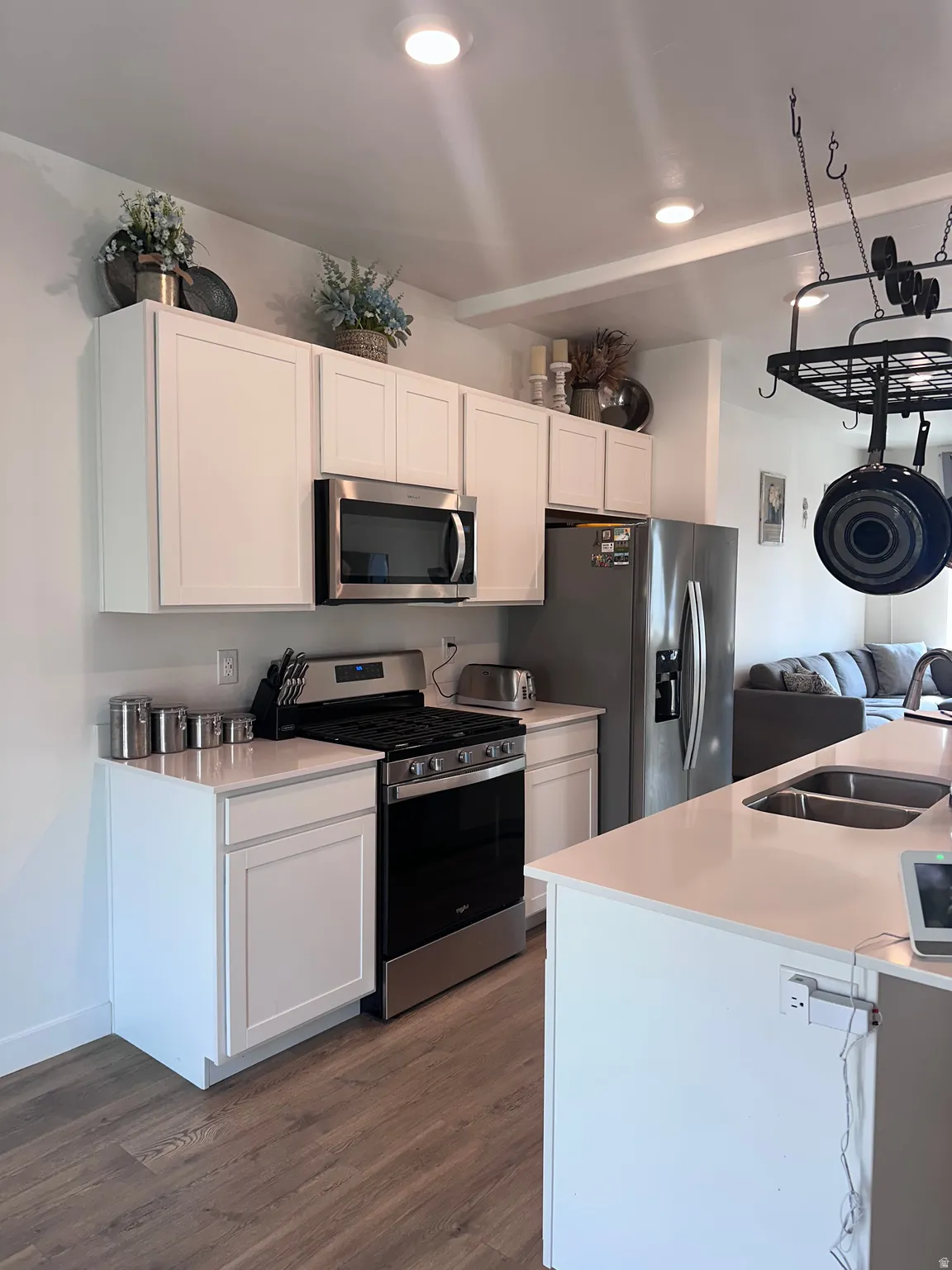 Contemporary kitchen featuring white cabinetry, stainless steel appliances, light-toned countertops, wood-finish flooring, and recessed ceiling lighting