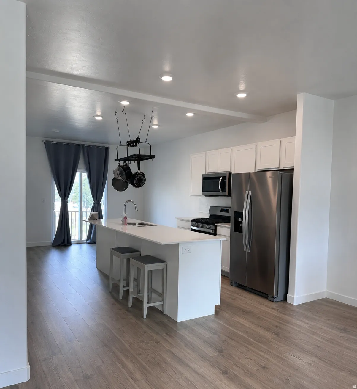 Contemporary kitchen and living area featuring wood-finish flooring, white cabinetry, stainless steel appliances, and an island with bar seating