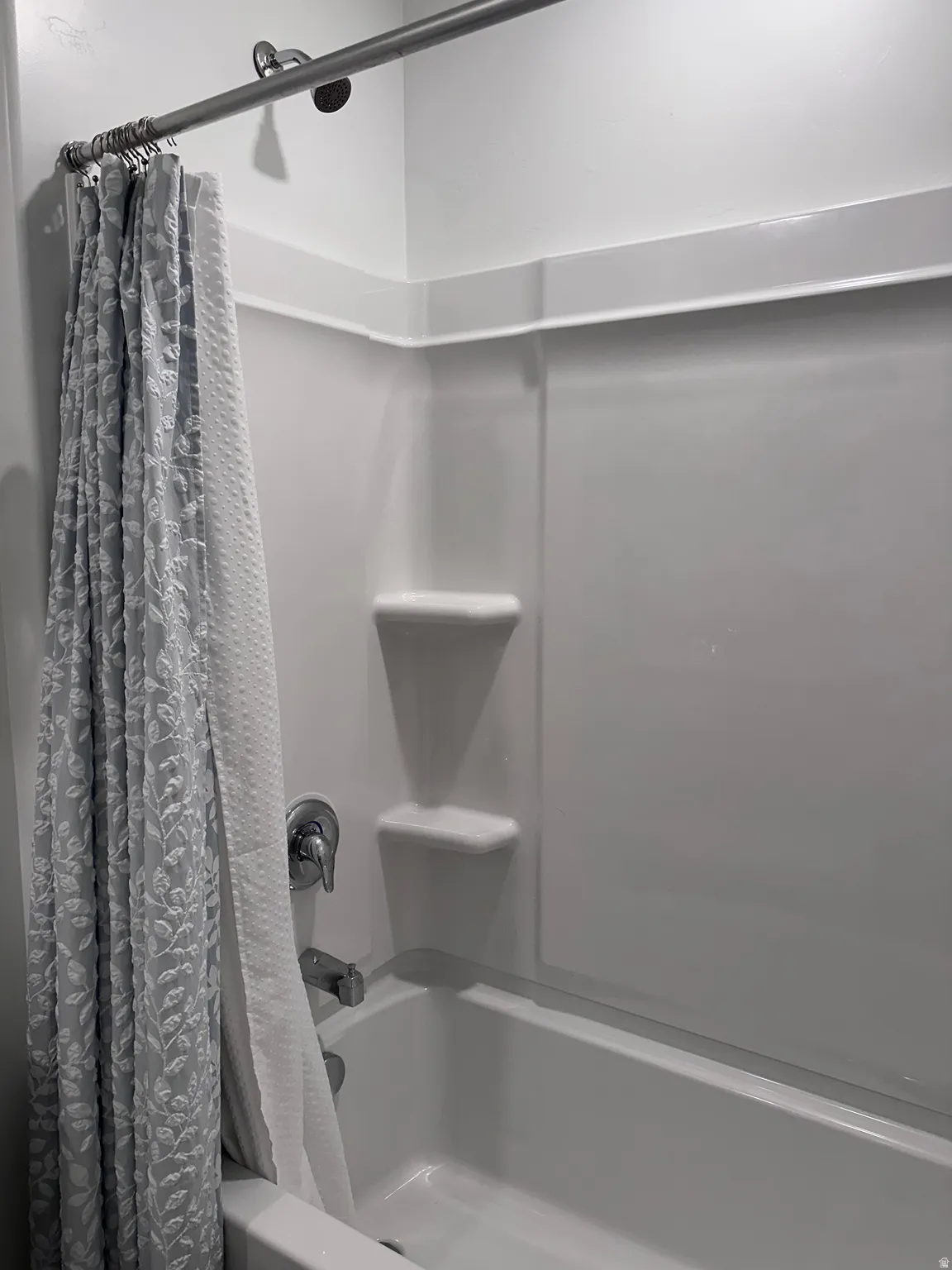 Bathtub shower combination with integrated shelving, chrome fixtures, and a white finish
