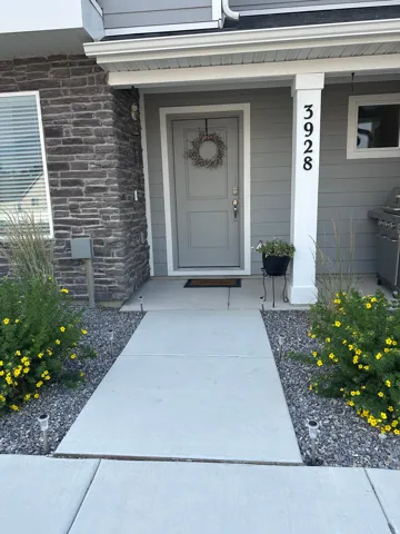 Entryway featuring a contemporary gray door, stone veneer accent wall, white trim, and a concrete pathway