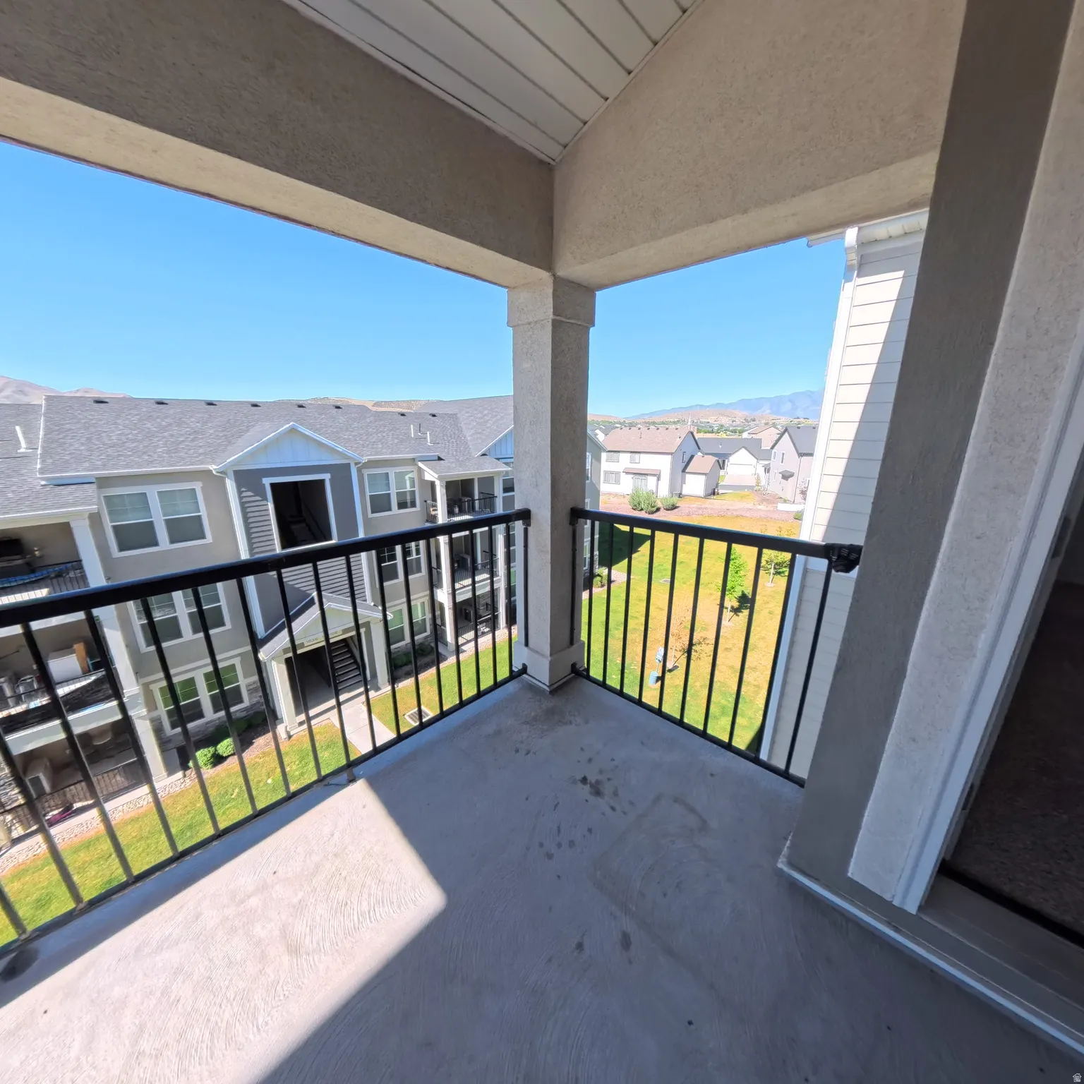 Exterior balcony with concrete flooring, black metal railing, and sturdy support columns