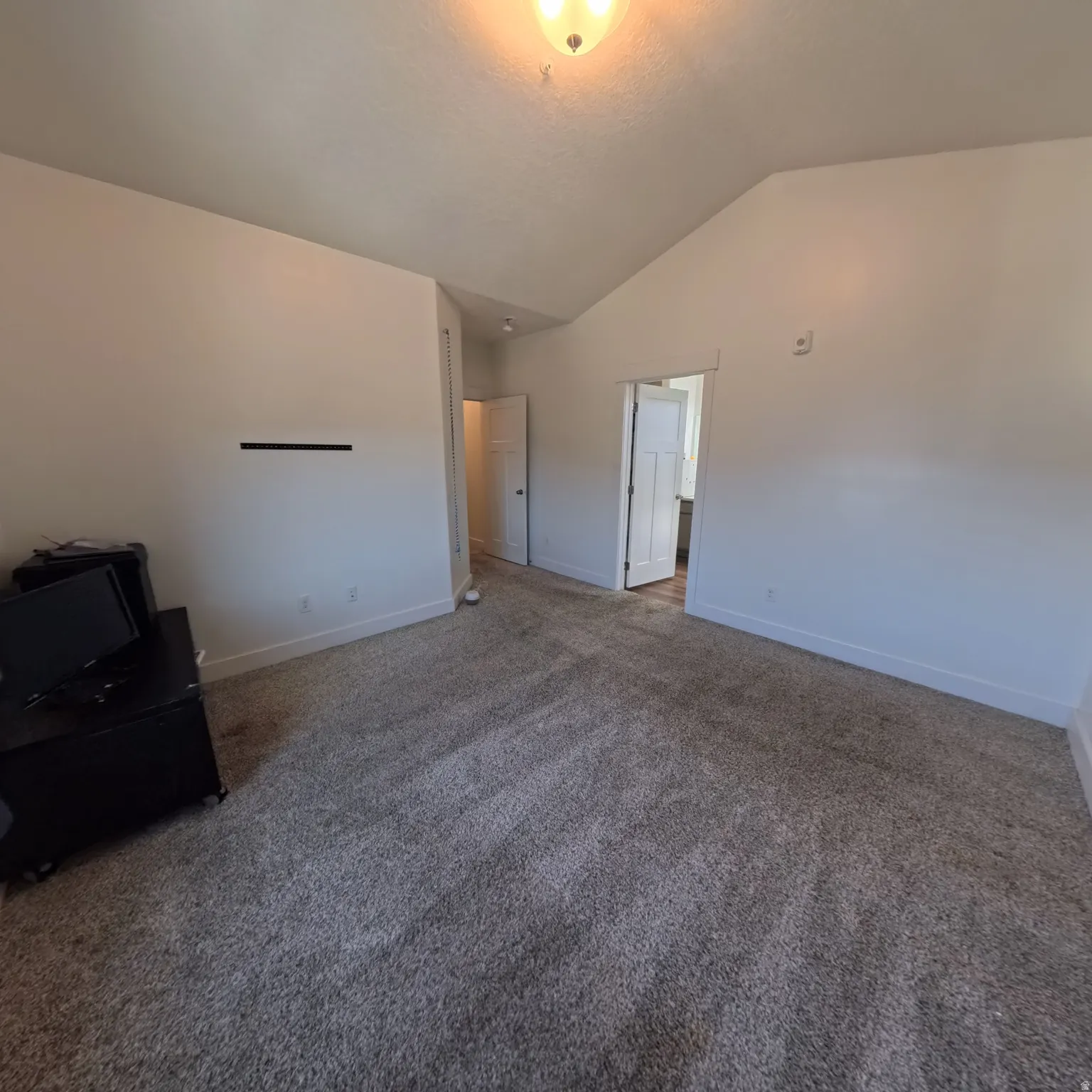 Spacious interior room featuring a vaulted ceiling and neutral wall tones
