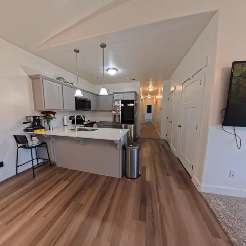 Kitchen featuring light gray cabinetry, stainless steel appliances, a white countertop island with seating, and wood-finish flooring