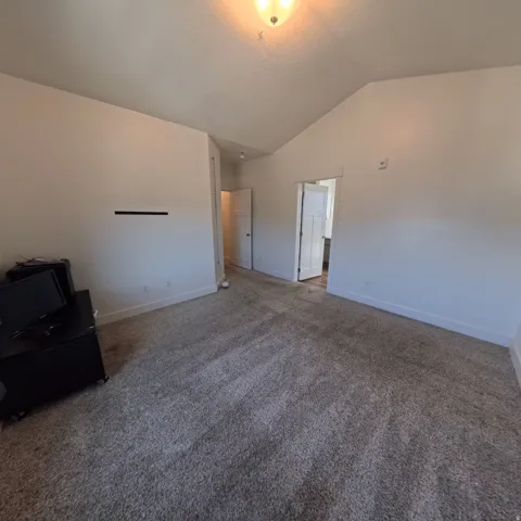 Spacious interior room featuring a vaulted ceiling and neutral wall tones