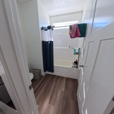 Bathroom featuring wood-finish flooring, a white bathtub with an integrated shower, and a high window for natural light
