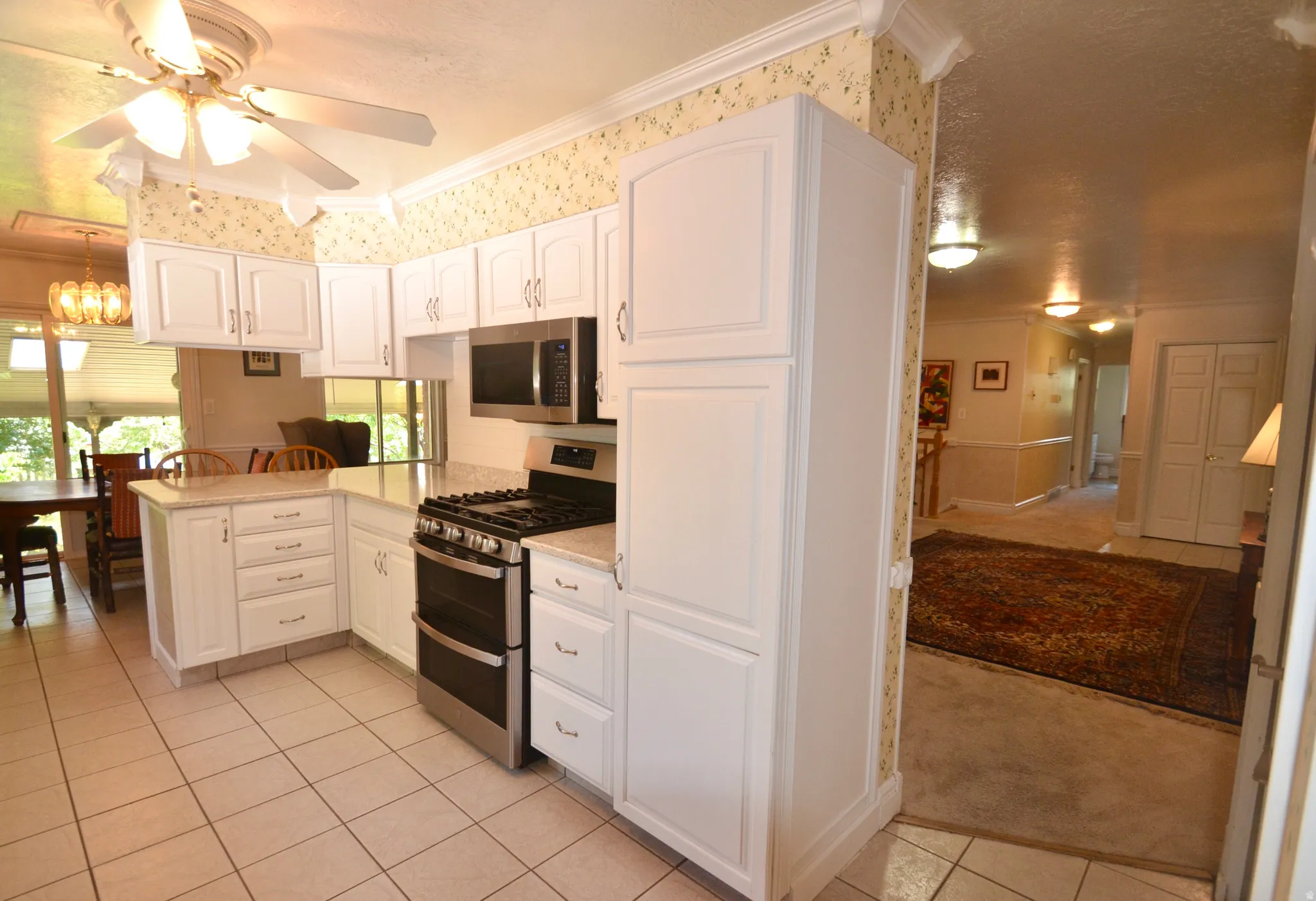 Kitchen featuring white cabinetry, light-toned countertops, tile flooring, stainless steel appliances, and a ceiling fan with integrated lighting