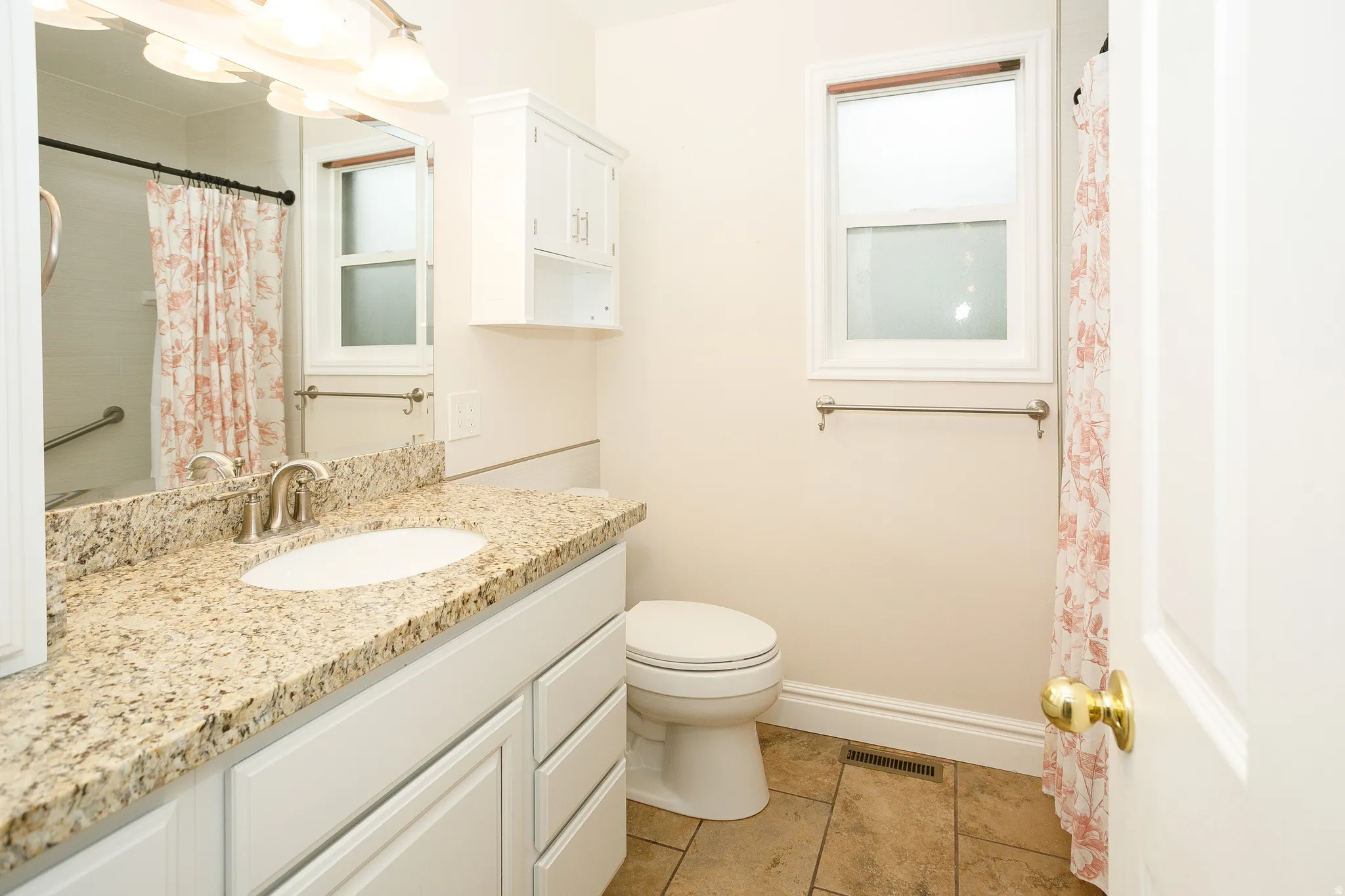 Bathroom featuring a single vanity with a speckled countertop, undermount sink, and brushed nickel faucet