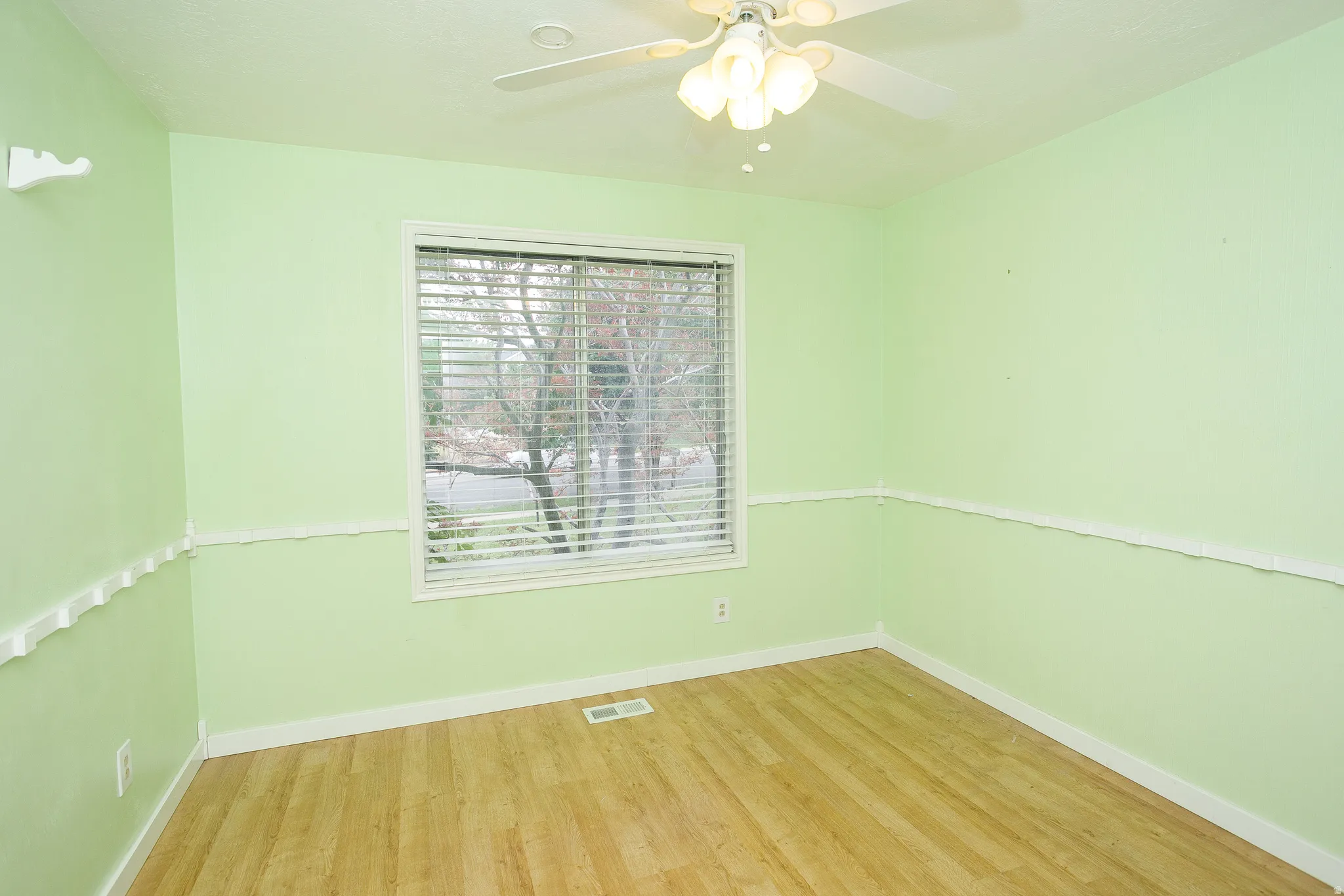 Room featuring wood-finish flooring, a large window with horizontal blinds, and a ceiling fan with integrated lighting